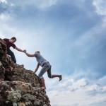 Rosa Media Productions - Man giving helping hand to friend to climb mountain rock cliff