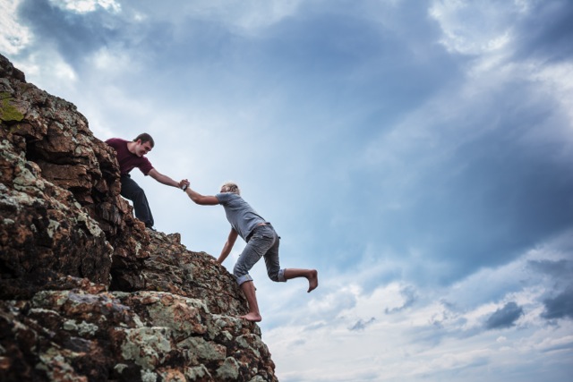 Rosa Media Productions - Man giving helping hand to friend to climb mountain rock cliff